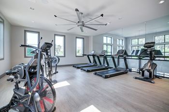 A gym with treadmills and weights and a ceiling fan